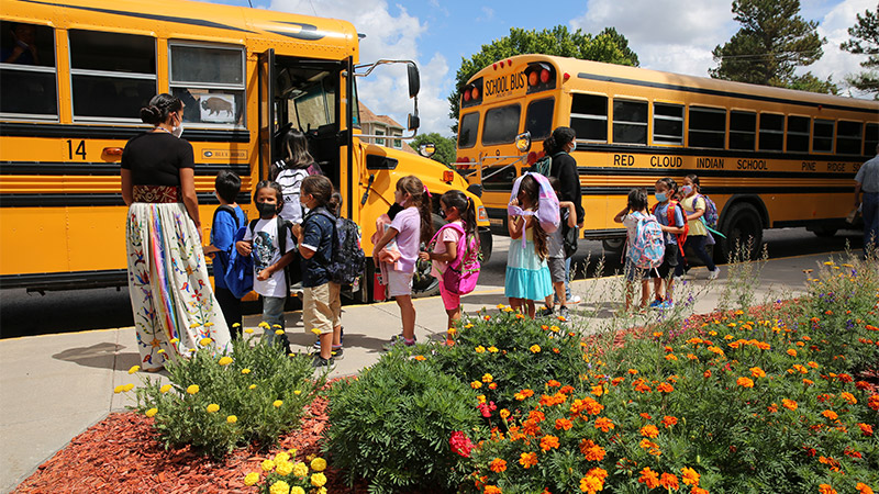 Outdoor photo of children in front of two school buses
